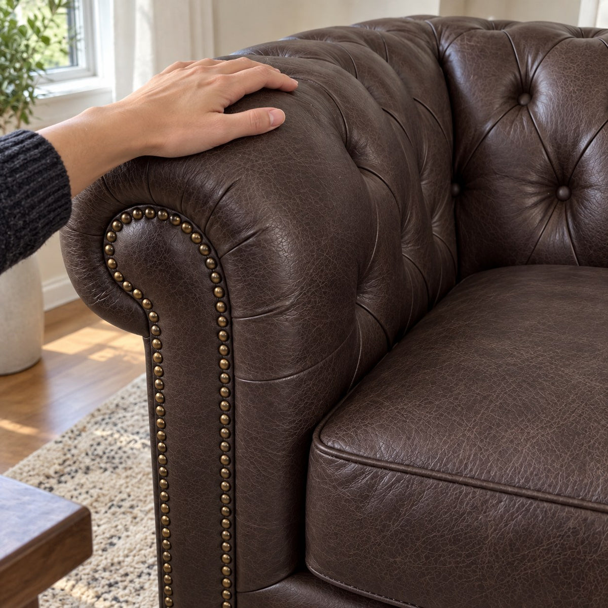Detalhe ilustrativo da textura do couro Café, capitonê e braço rolô com mão apoiada